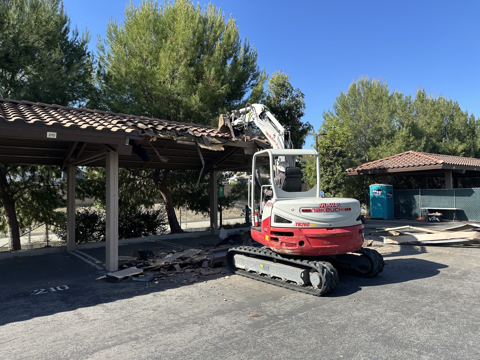 Mini excavator taking down a parking lot carport