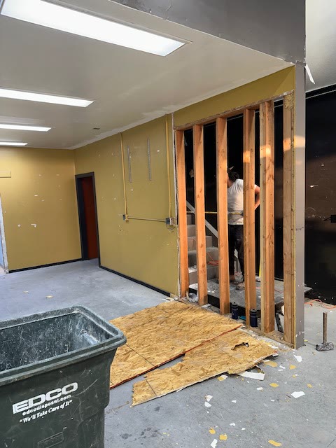 Interior wall opened to framing during commercial demolition with debris bin staged