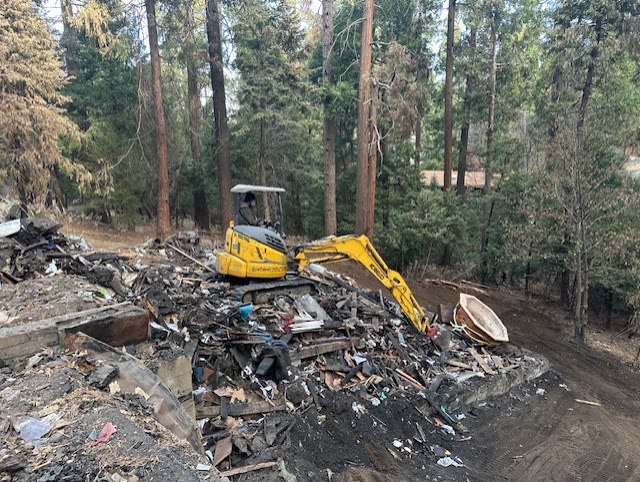 Excavator demolishing burnt house structure in Crestline, San Bernardino County